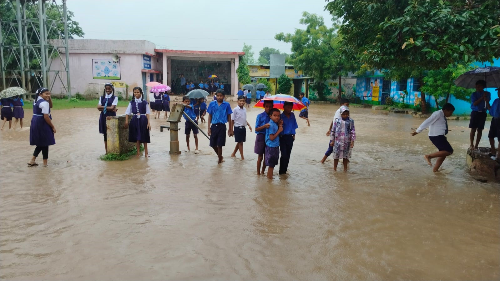 शासकीय प्राथमिक व माध्यमिक स्कूल परिसर कलारतराई में भरे पानी पर चलते हुए विद्यार्थी।