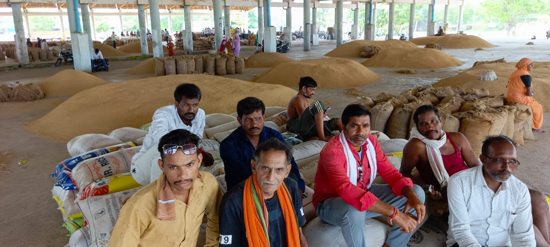 श्यामतराई कृषि उपज मंडी में बैठे हुए किसान, पीछे रखी धान की ढेरी। श्यामतराई कृषि उपज मंडी में बैठे हुए किसान, पीछे रखी धान की ढेरी।
