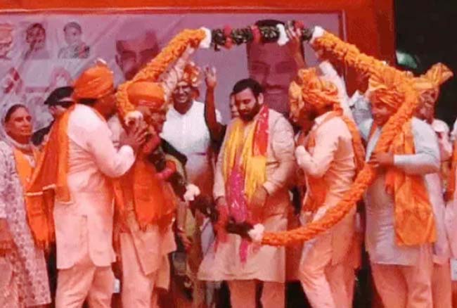 23 Snp-     सोनीपत: कार्यकारी मुख्यमंत्री के काफिले         पर पुष्प वर्षा करते हुए ग्रामीण। मंच पर नायब सेनी का स्वागत करते हुए कार्यकर्ता