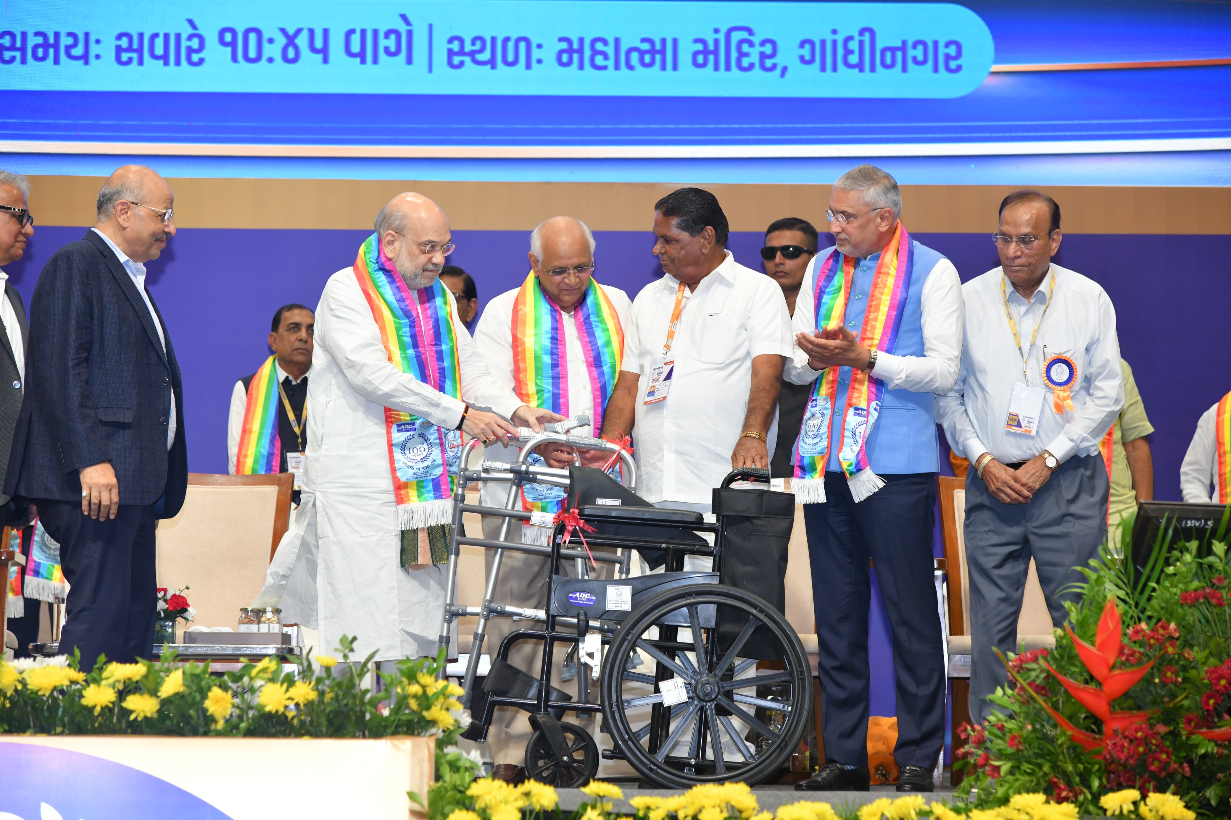 केंद्रीय सहकारिता मंत्री अमित शाह शुक्रवार को गांधीनगर के महात्मा मंदिर में एडीसी बैंक के स्वर्णिम शताब्दी महोत्सव में बैंक से जुड़े सेवा सहकार मंडली के सभासद को व्हील चेयर देते हुए।