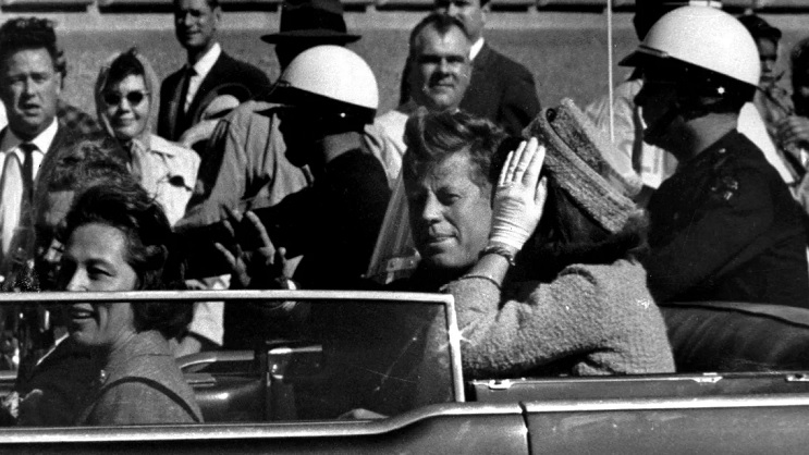 अमेरिका के पूर्व राष्ट्रपति जॉन एफ. कैनेडी 22 नवंबर 1963 को गोली मारे जाने से लगभग एक मिनट पहले अपनी कार के काफिले में हाथ हिलाते हुए। अमेरिका के पूर्व राष्ट्रपति जॉन एफ. कैनेडी 22 नवंबर 1963 को गोली मारे जाने से लगभग एक मिनट पहले अपनी कार के काफिले में हाथ हिलाते हुए।