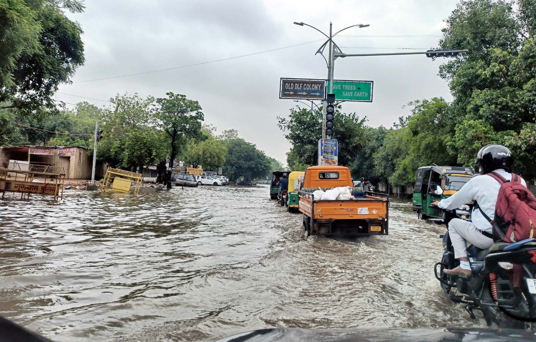 गुरुग्राम में पुराना दिल्ली रोड पर भरे बरसाती पानी से गुजरते वाहन।