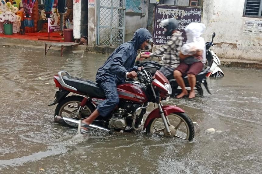 शहर की गलियों में अधिक पानी भरने के कारण बाइक चालक फंसे।