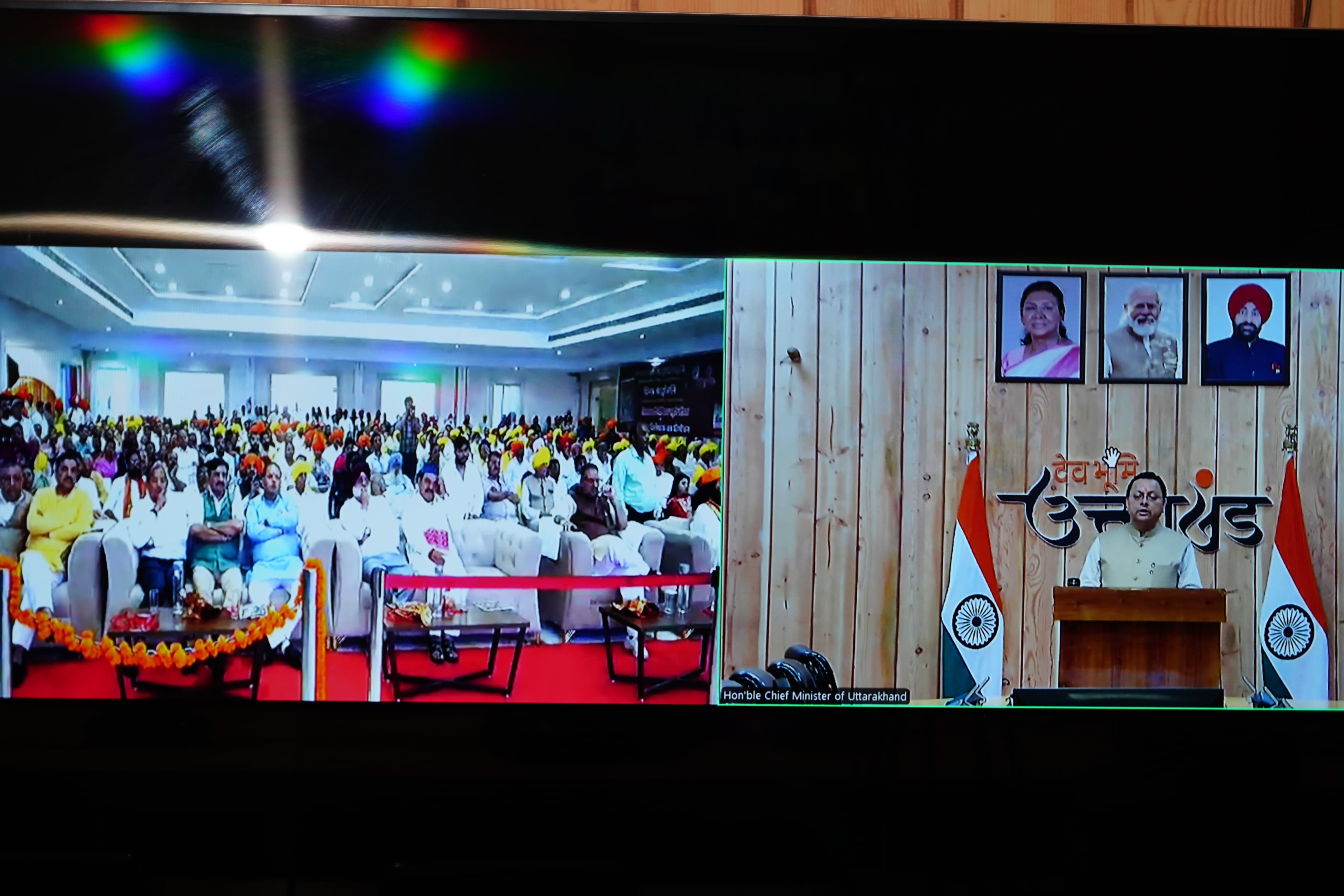 काशीपुर में विभाजन विभीषिका स्मृति दिवस के अवसर पर आयोजित कार्यक्रम में उपस्थित लोग और मुख्यमंत्री वर्चुअल संबोधित करते।