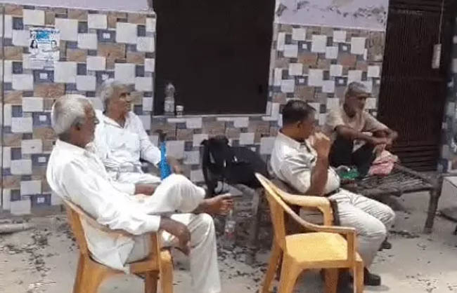 गली में बैठे पुलिस कर्मी व लोग।